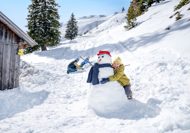     Zábava na snehu v Alpbachtali, rodina pri stavaní snehuliaka 